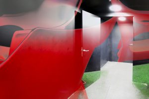 Galerie Ahlemann zeigt ein abstraktes Foto von Petra Jaenicke welches durch die Farbe Rot dominiert wird. Das Foto zeigt einen leeren Raum mit einer offenen Tür, die in einen Flur führt. Das Foto ist surreal verfremdet durch überwiegend rote Farbelemente, die wie Graffitis wirken, aber über alle Raumelemente hinweg "aufgesetzt"sind.
