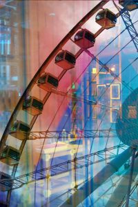 Galerie Ahlemann zeigt ein abstraktes Foto der Fotokünstlerin Hasina Khan auf dem in verschiedenen Farben ein Ausschnitt des Hngkonger Riesenrades zu sein ist, kollagiert mit Hongkonger Häuserfassaden im Hintergrund.