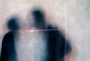 Galerie Ahlemann zeigt ein abstraktes Foto von Ingrid Pohl aus der Konzeptreihe "Adoleszenz" auf dem schemenhaft zwei Personen hinter einer Milchglasscheibe zu sehen sind.