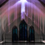 Galerie Ahlemann zeigt ein abstraktes Foto von Ingrid Pohl aus der Konzeptreihe "Zwischen Zeiten", das einen mit Bauplanen abgehangenen Deckengewölbebogen vor einem dreiteiligen Kirchenfenster darstellt.