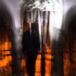 Galerie Ahlemann zeigt ein abstraktes Foto von Ingrid Pohl aus der Konzeptreihe "Zwischen Zeiten" auf dem in einer unscharfen Darstellung eine Person vor großen, orange leuchtenden Kirchenfenstern zu sehen ist.