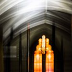 Galerie Ahlemann zeigt ein abstraktes Foto von Ingrid Pohl aus der Konzeptreihe "Zwischen Zeiten" auf dem ein Ausschnitt einer Kirchendecke mit Gerüststangen vor einem orange leuchtenden Kirchenfenster zu sehen ist.