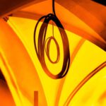Galerie Ahlemann zeigt ein abstraktes Foto von Ingrid Pohl aus der Konzeptreihe "Zwischen Zeiten" auf dem in orangen und gelben Farbtönen ein eingerolltes Elektrokabel an der Decke eines Kirchengewölbes hängt.