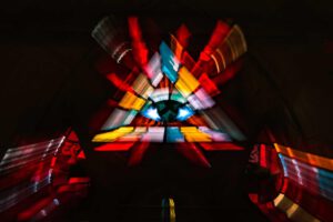 Galerie Ahlemann zeigt ein abstraktes Foto von Ingrid Pohl aus der Konzeptreihe "Zwischen Zeiten" auf dem ein buntes dreieckiges Kirchenfenster in abstrahierter Darstellung zu sehen ist.
