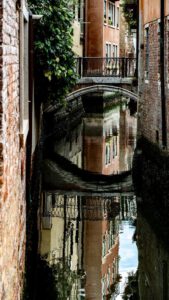 Galerie Ahlemann zeigt ein Foto des Fotokünstlers Mick Schäfer aus der Serie "Reflecting Venice" auf dem eine kleine Brücke in einer Häuserschlucht mit deren Wasserreflektion zu sehen ist.