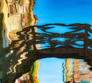 Galerie Ahlemann zeigt ein Foto des Fotokünstlers Mick Schäfer aus der Serie "Reflecting Venice" auf dem die verzerrte Wasserspiegelung einer Holzbrücke zu sehen ist.